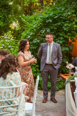 Wedding guests chatting at an outdoor garden reception with white chairs and lush greenery.
