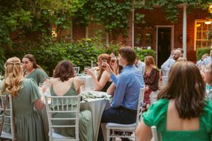 Guests seated at tables enjoy an elegant outdoor reception under green foliage at dusk.