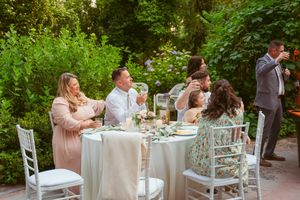 Garden party reception with white chairs and tables arranged under leafy trees.
