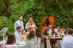 Intimate outdoor wedding reception with guests seated at white tables among natural garden surroundings.