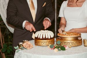 Wedding couple cutting into gold-decorated wedding cakes with ornate designs at an elegant reception celebration.