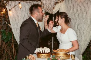 Couple laughing while feeding each other cake at their rustic outdoor wedding reception.