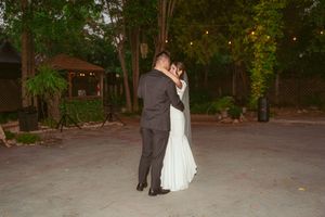 A couple shares a romantic first dance at dusk under string lights in an outdoor wedding venue.