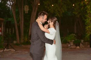 A couple embraces during their first dance at an intimate outdoor evening wedding reception.