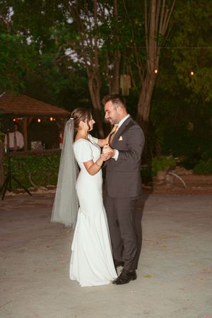 Couple sharing their first dance under string lights at an outdoor wedding venue.