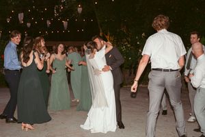 Wedding celebration with bridesmaids in green dresses dancing on an outdoor patio at night under string lights.