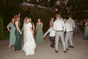 Wedding party in sage green dresses mingling on the dance floor at outdoor reception.