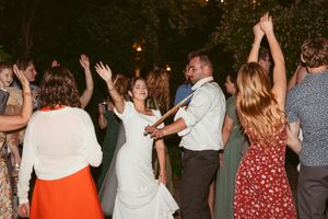 Wedding guests dance with their hands raised on a dark dance floor illuminated by warm overhead lighting.