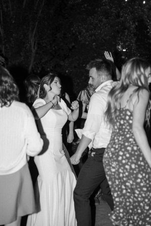 Black and white photo of people dancing at what appears to be a wedding reception or party with festive energy.