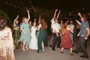 Wedding guests dance and celebrate on an outdoor dance floor illuminated by string lights at night.