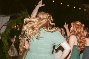 People in mint green dresses dancing at an outdoor party with string lights hanging above.