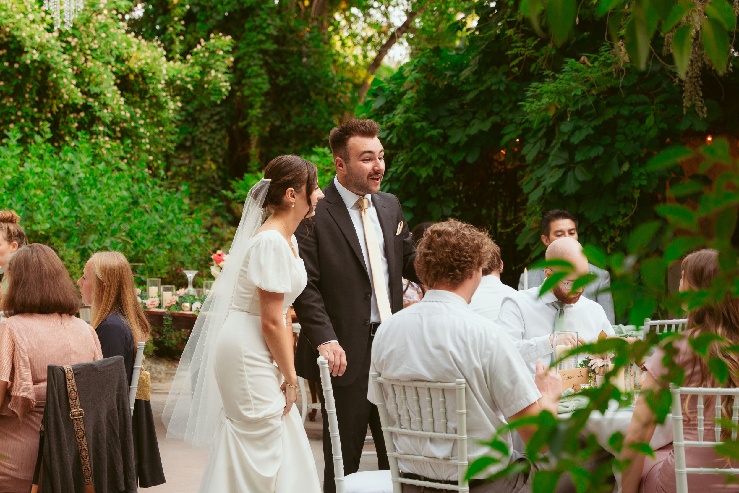 Outdoor garden wedding reception with white chiavari chairs and elegant table settings surrounded by greenery.