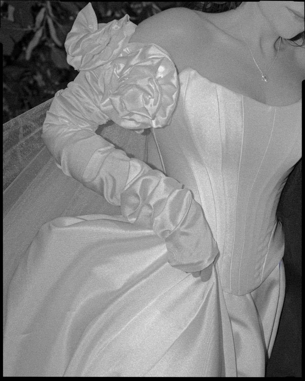 Black and white photo of a bride in a satin corset wedding gown with ruffled gloves and floral detail.