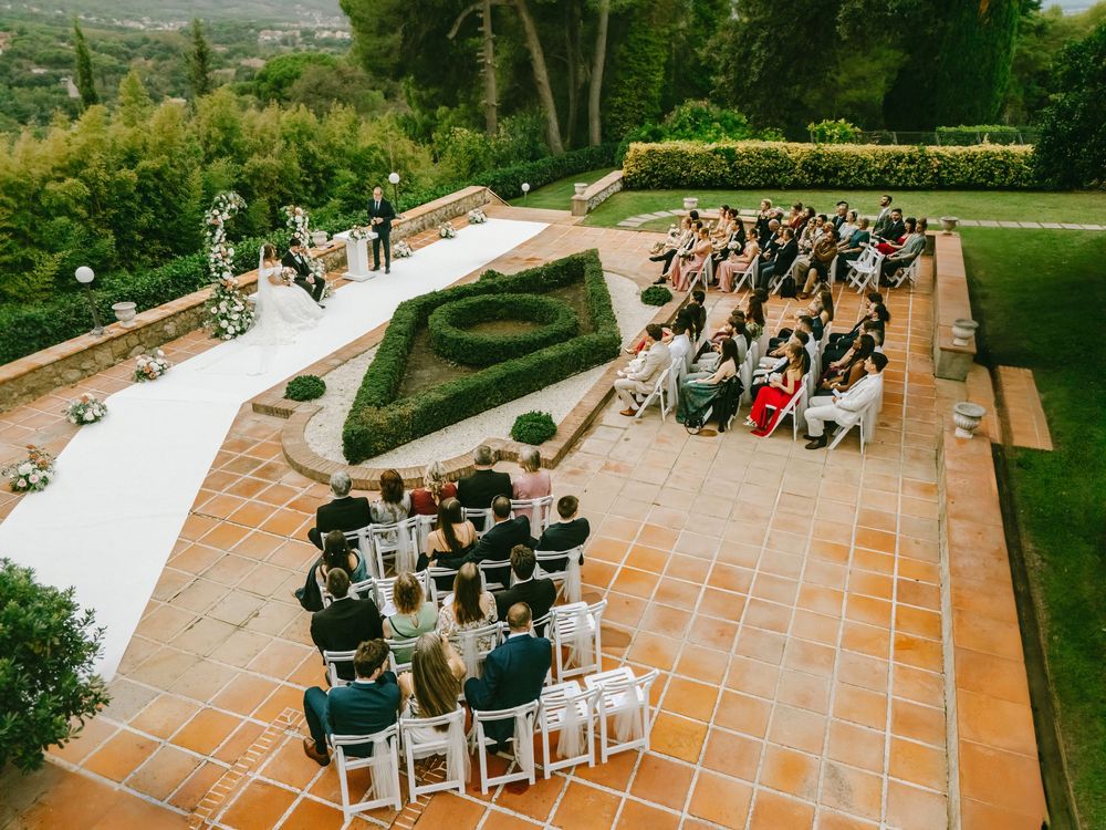 Aerial view of an elegant outdoor wedding ceremony in a formal garden with terracotta tiles and lush greenery.