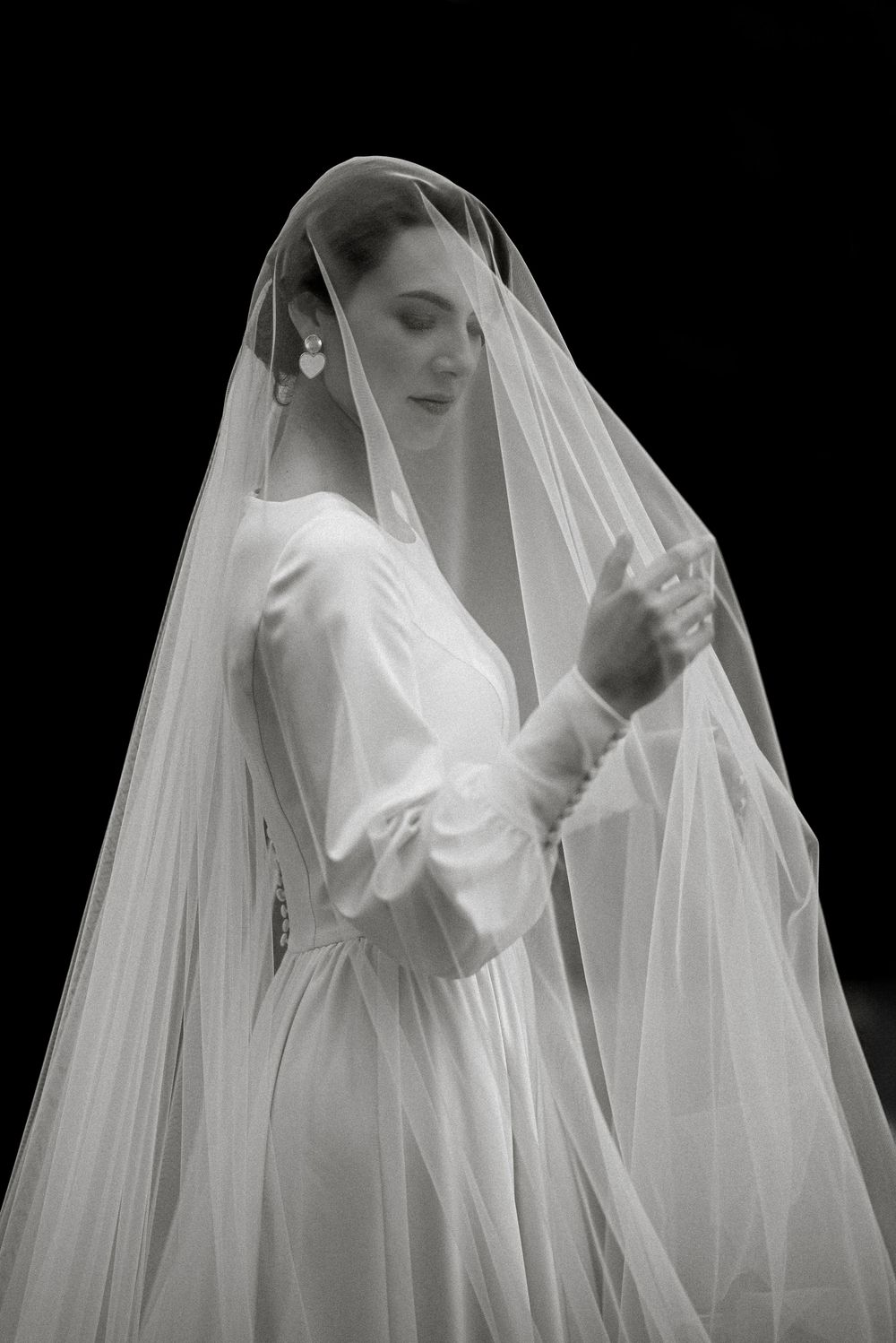 Elegant bride in white wedding gown and flowing veil, black and white portrait photography.