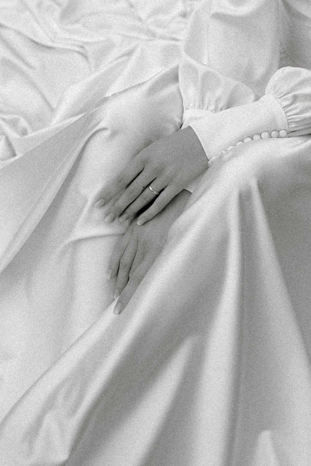 Close-up of a bride's hands resting on a flowing white satin wedding dress, wearing a delicate ring.