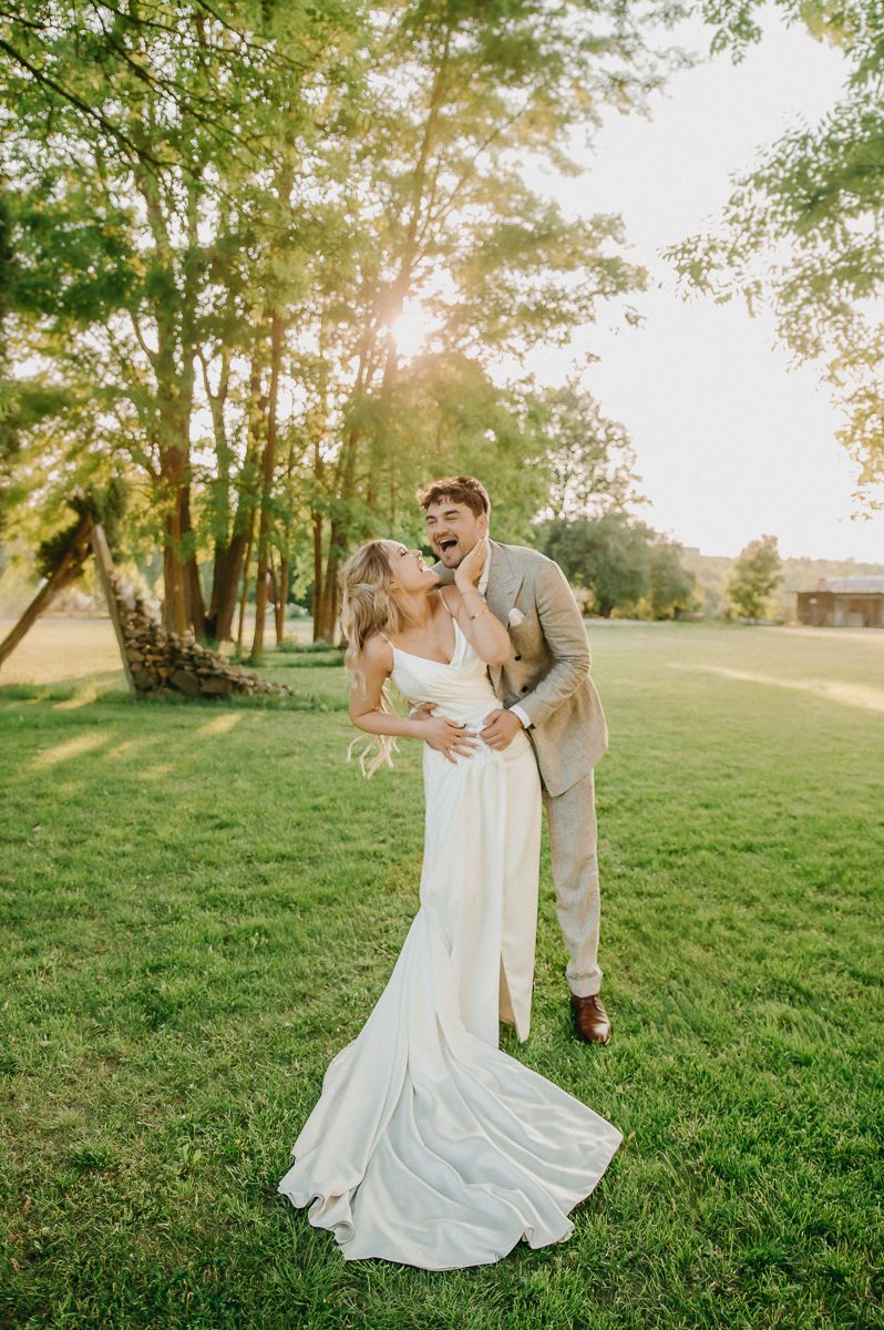 Couple dancing joyfully on a grassy hill during golden hour at their outdoor wedding celebration.
