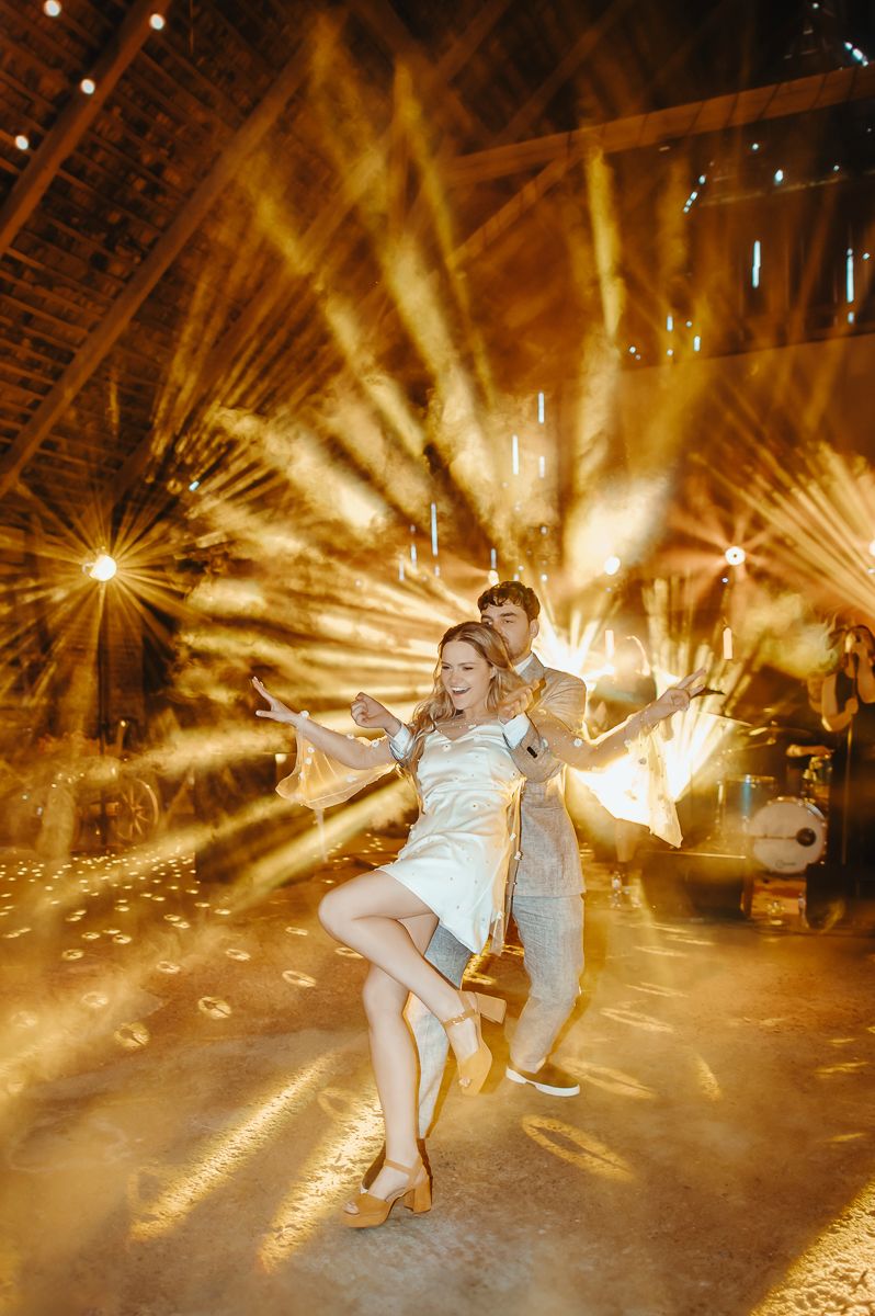 Dancing couple leaps dramatically on dance floor as golden stage lights create dramatic sun-like burst effects behind them.