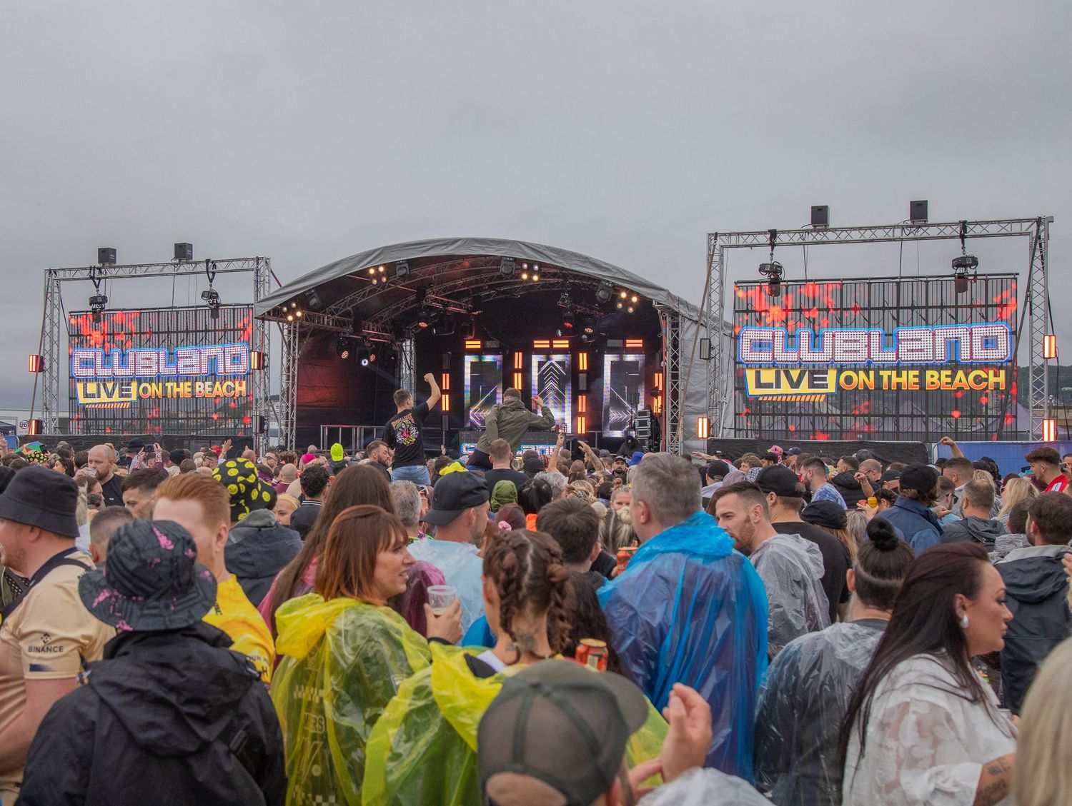 Large crowd of festival-goers in rain gear watching a performance at an outdoor music festival stage.