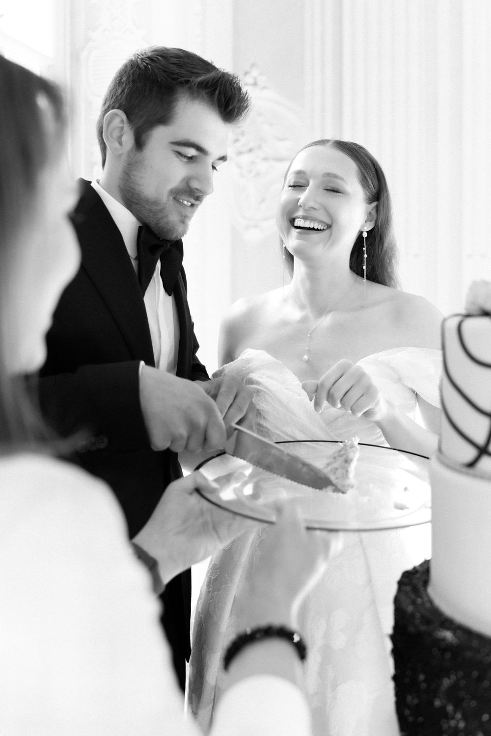 Black and white photo of newlyweds joyfully cutting their wedding cake together at the reception.