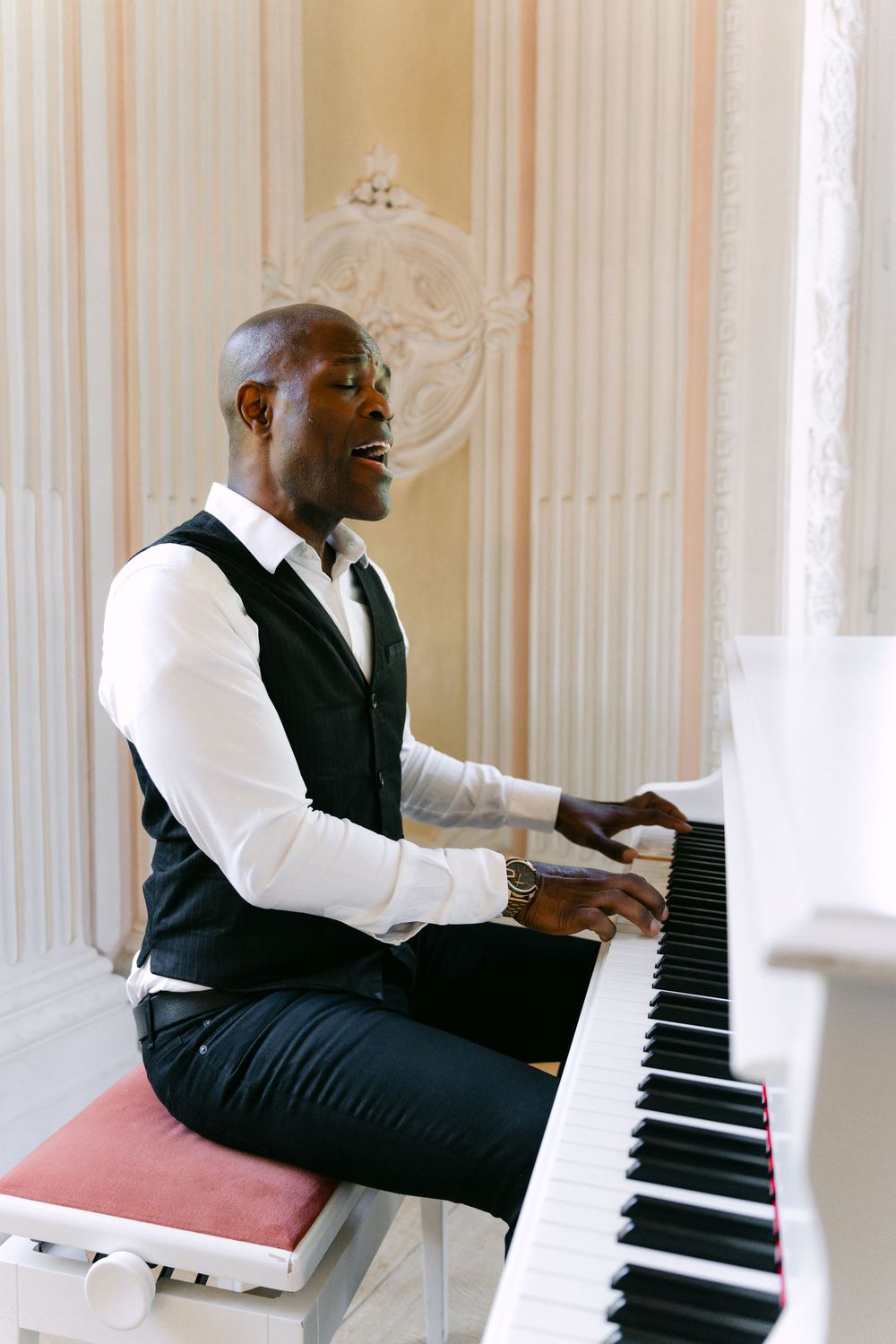 Musician in formal attire performs on white grand piano in elegant room with striped wallpaper.