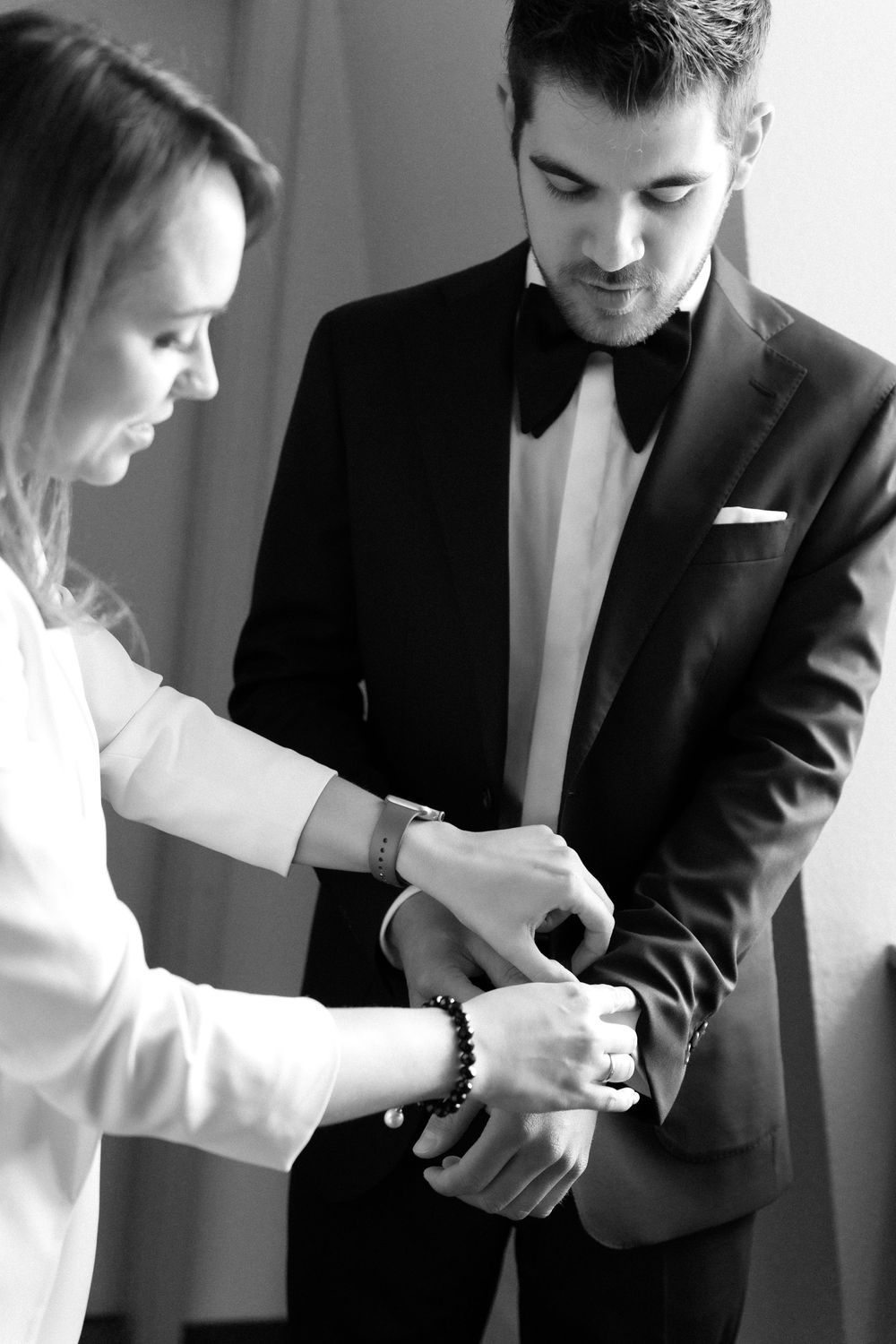 Black and white photo showing someone helping adjust formal wear cufflinks and sleeve on a tuxedo jacket.