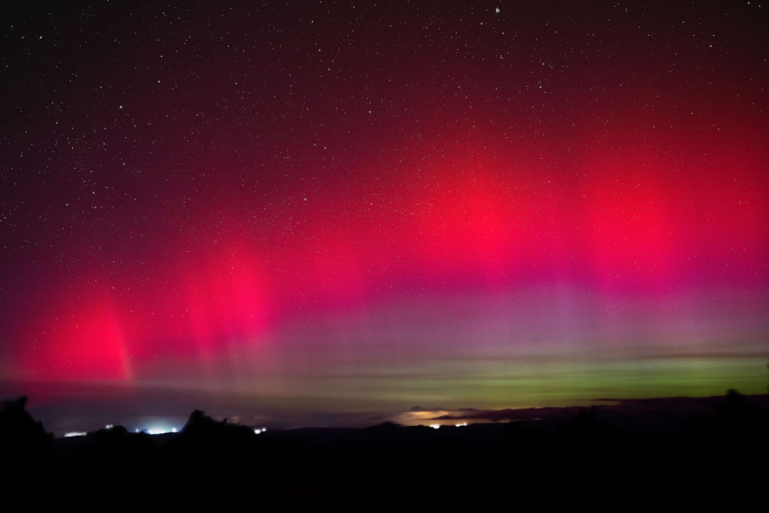Aurore boréale rouge et violette illuminant le ciel nocturne au-dessus d’un paysage sombre.