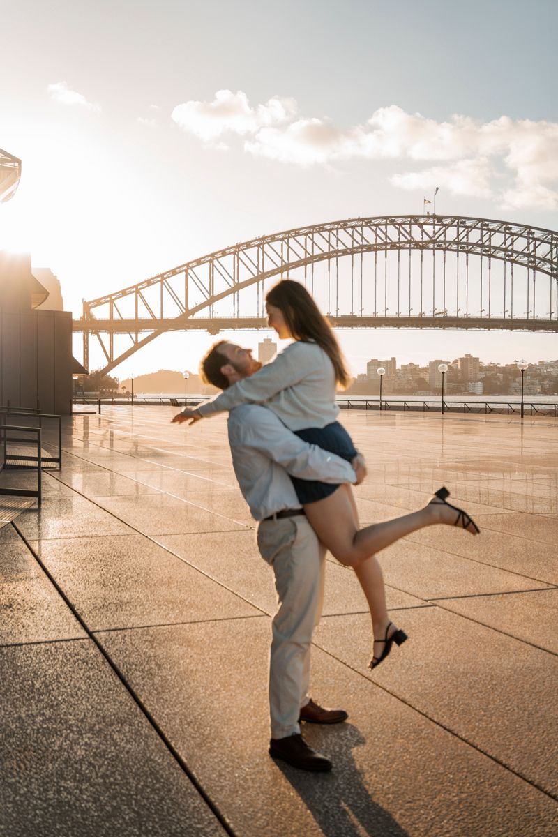 background in focus while man picks up her girlfriend in the golden light proposal photoshoot in Sydney