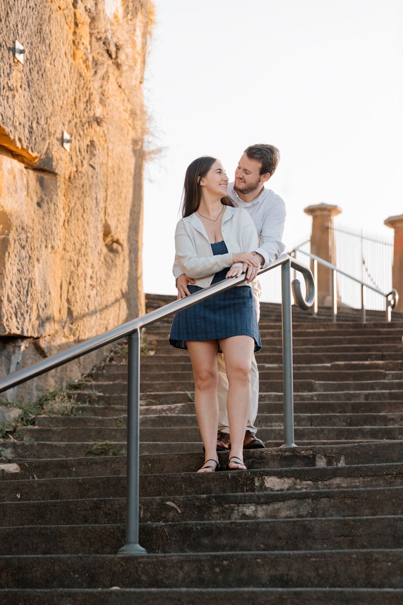 couple hugging on the stairs down near the Sydney Opera house during a proposal photoshoot in Sydney