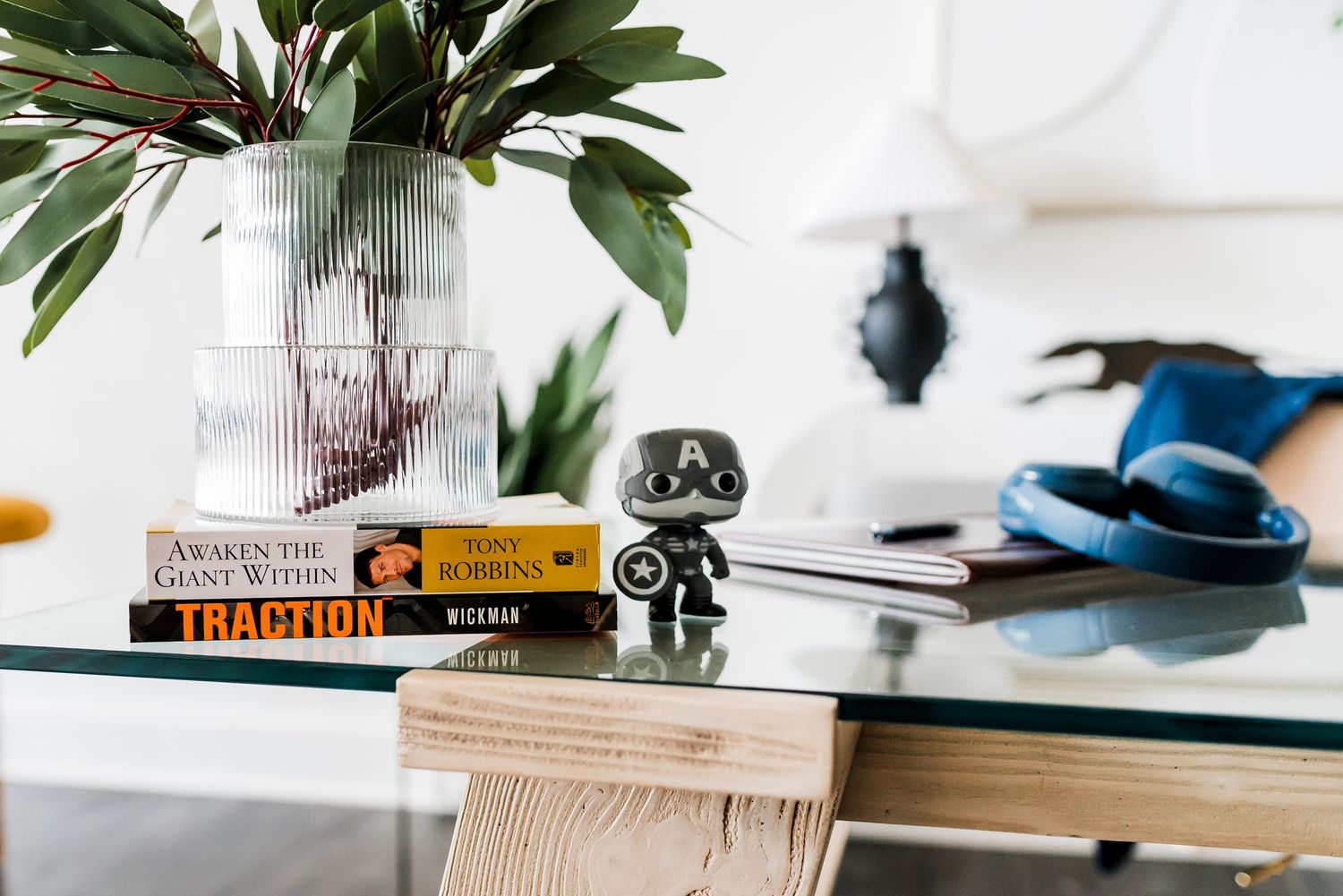 Small figurine and books displayed on white desk next to a vase with green leaves and office supplies.