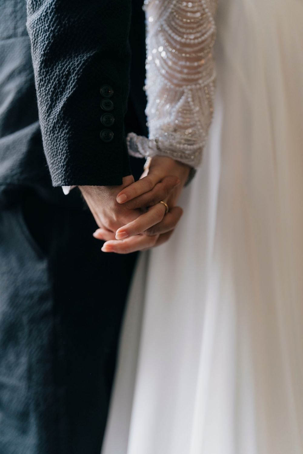 Close-up of couple holding hands showing wedding rings and lace sleeve detail.