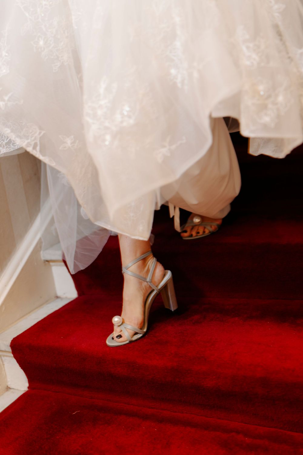 White wedding dress and elegant heels captured in detail against a luxurious red carpet.