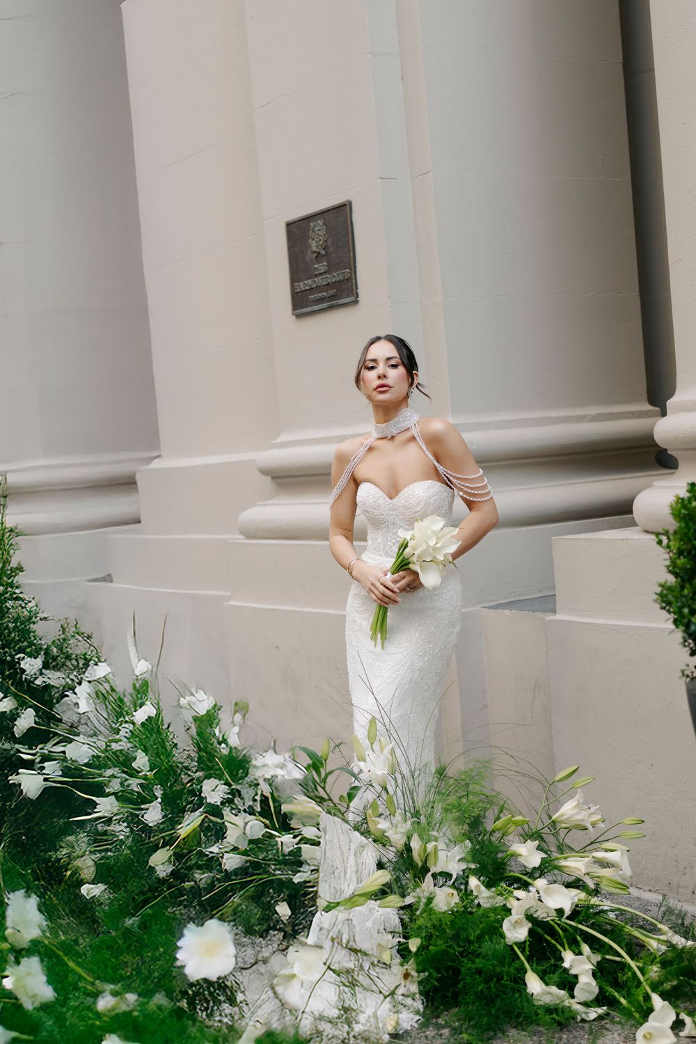 Elegant bridal portrait with white bouquet against classical architecture and floral decorations.