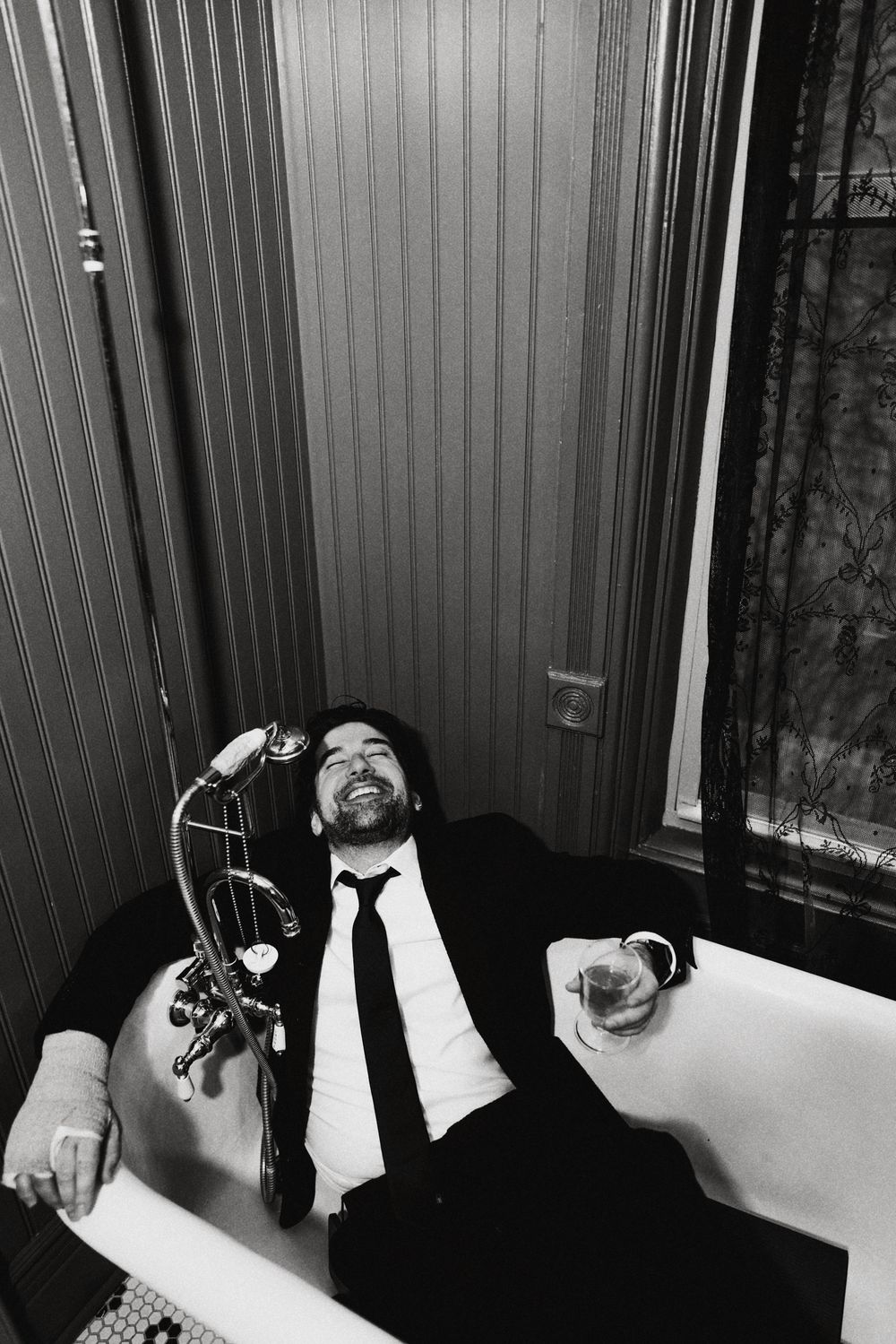 Black and white portrait of person in suit reclining with cocktail glass.