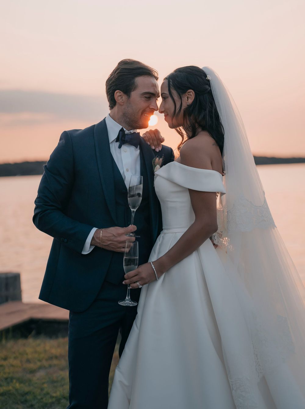 Newlyweds sharing champagne and intimate moments during sunset waterfront reception.