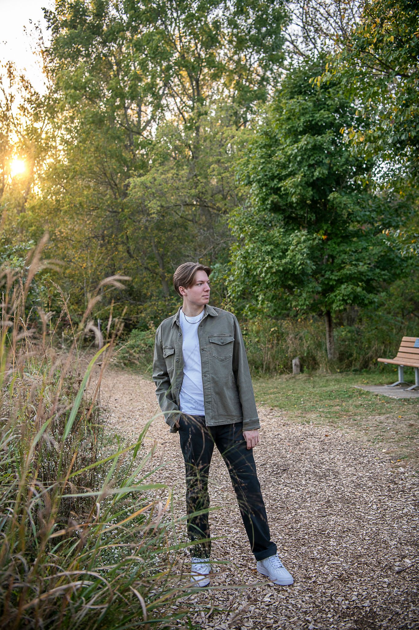 A person stands on a peaceful forest trail at sunset with golden light filtering through the trees.
