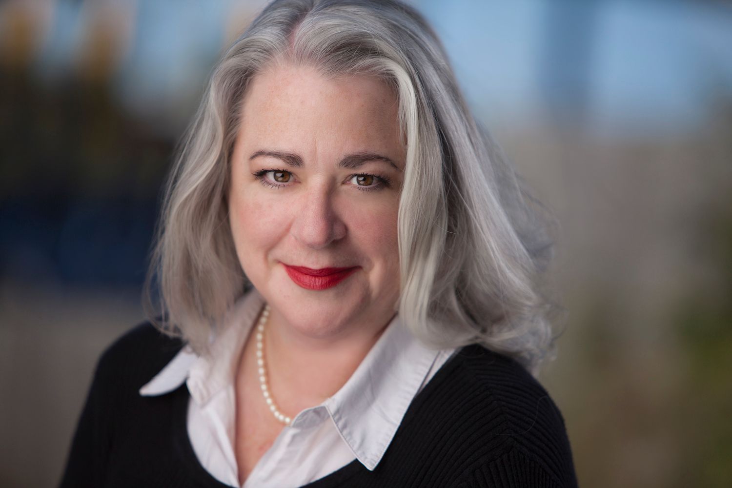 Professional headshot with person in black cardigan and white blouse with pearl necklace.
