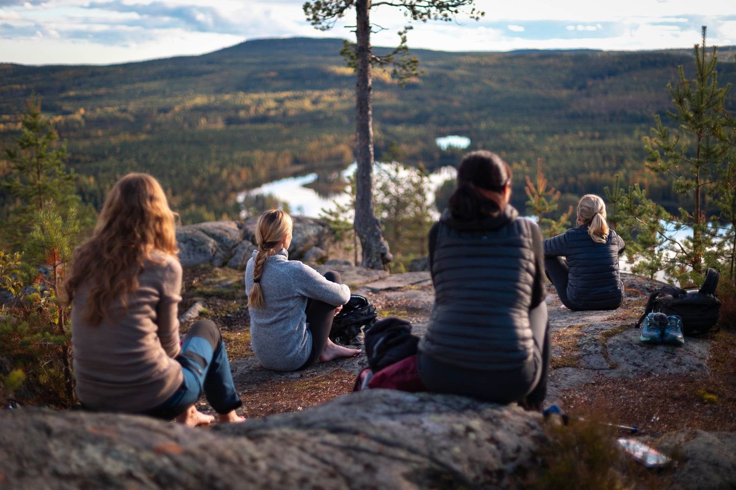 Group of women sitting on rocky overlook enjoying scenic forest and lake autumn view.