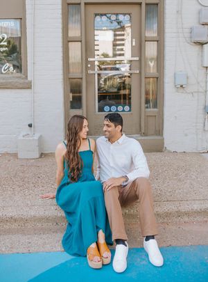 A couple sits together on a blue surface in front of a vintage doorway wearing coordinated casual outfits.