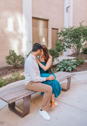 A couple shares an intimate moment while sitting on a bench surrounded by greenery and columns.