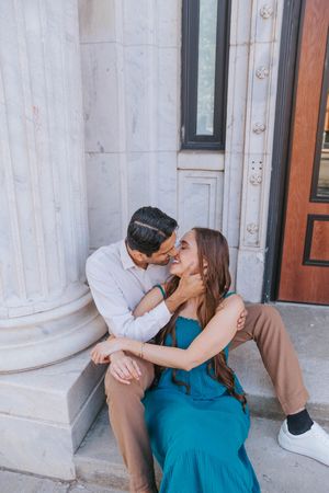 A couple shares a tender moment while sitting on stone steps near classical architecture columns.