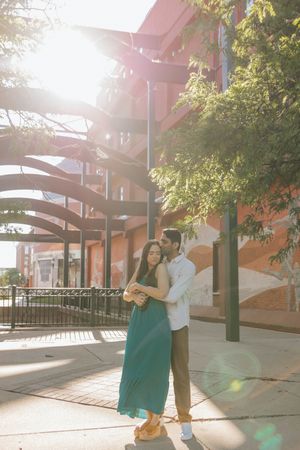 A couple embraces under sunlit architectural arches with trees providing natural framing.