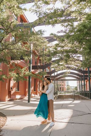A couple shares a romantic moment under arched walkways with dappled sunlight filtering through trees.