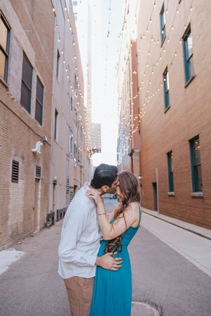 A couple embraces and kisses in an urban alleyway with brick walls on both sides.