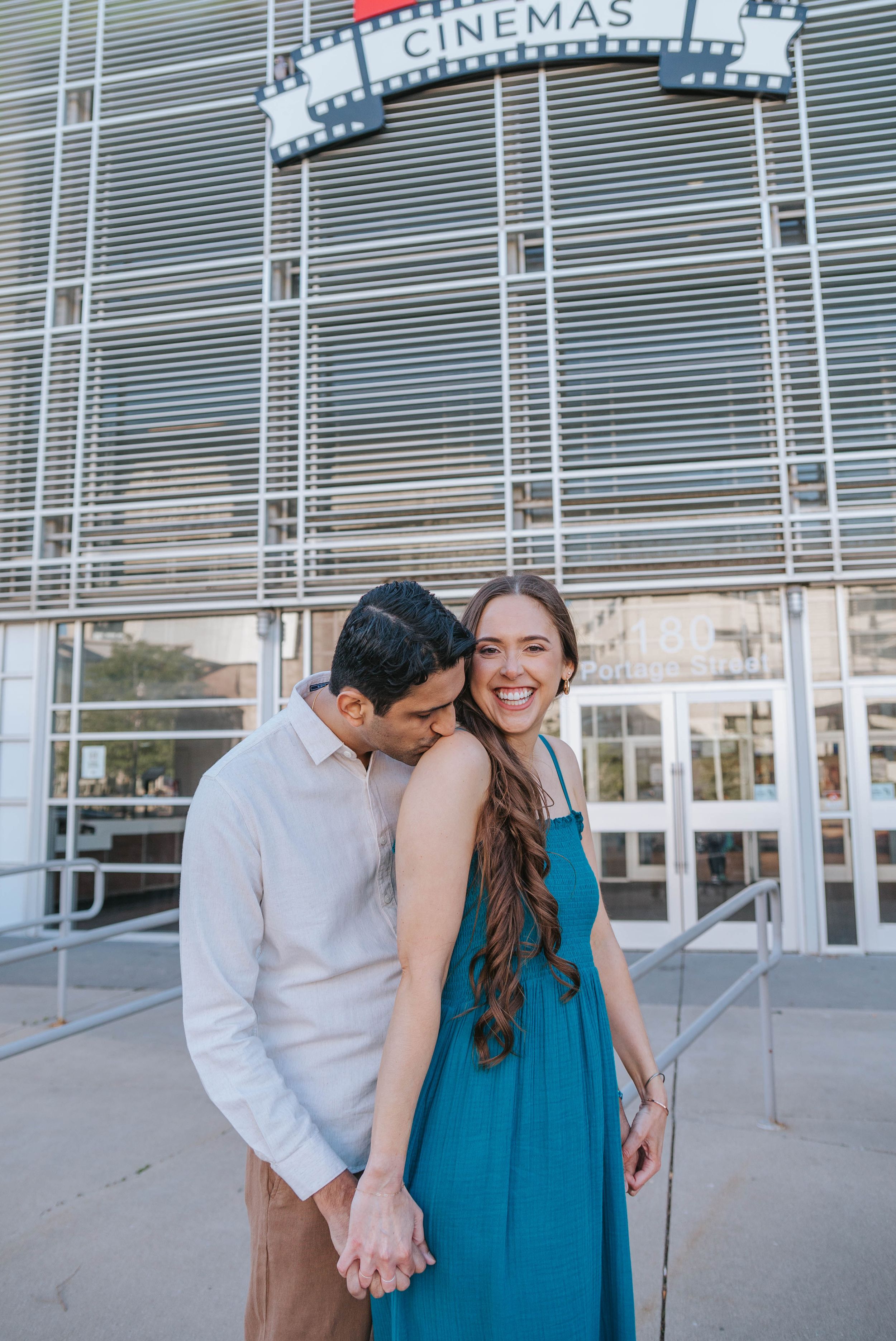 A couple shares playful moments outside a movie theater entrance.