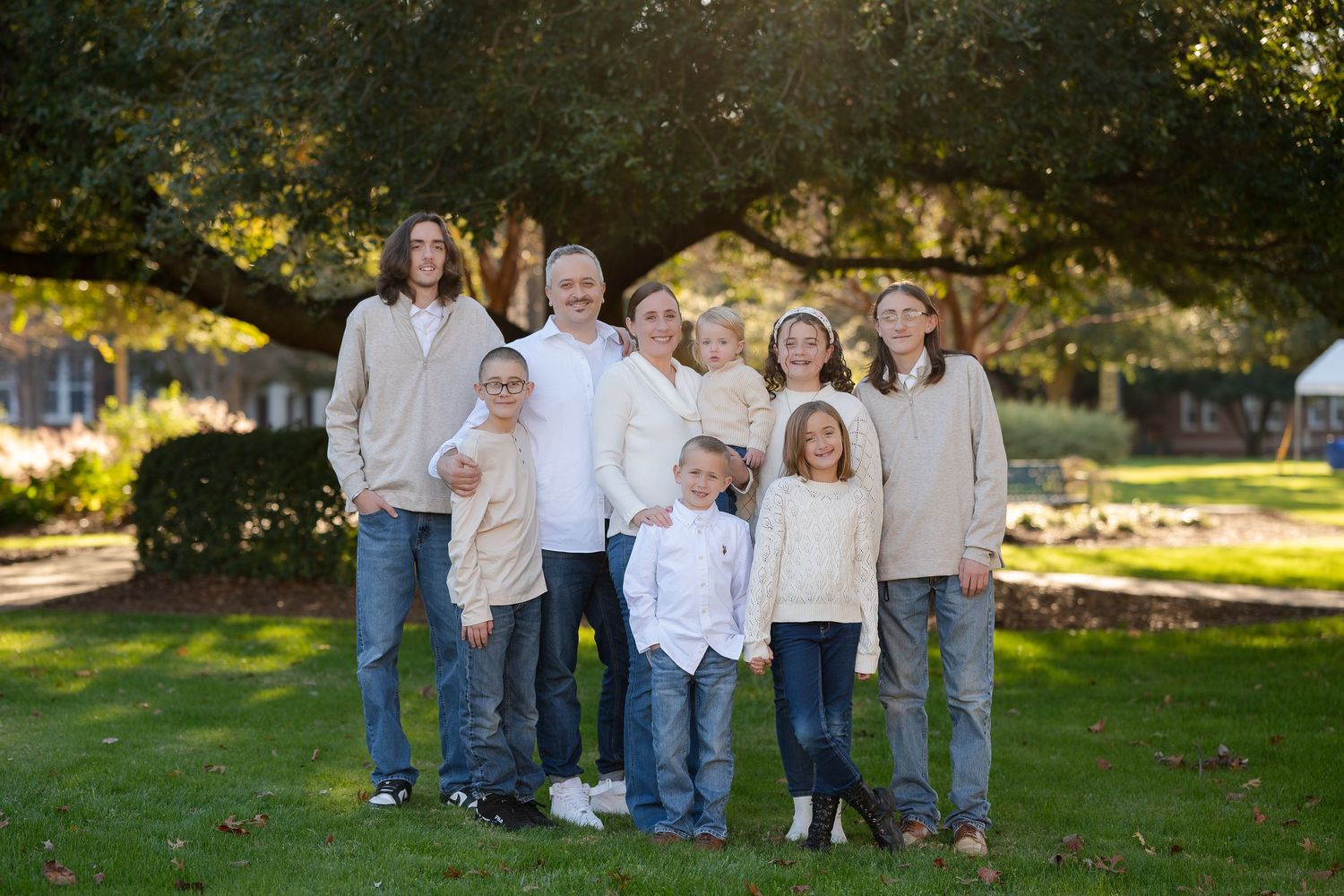A family group dressed in coordinating cream and blue casual clothing poses together on a sunny lawn.