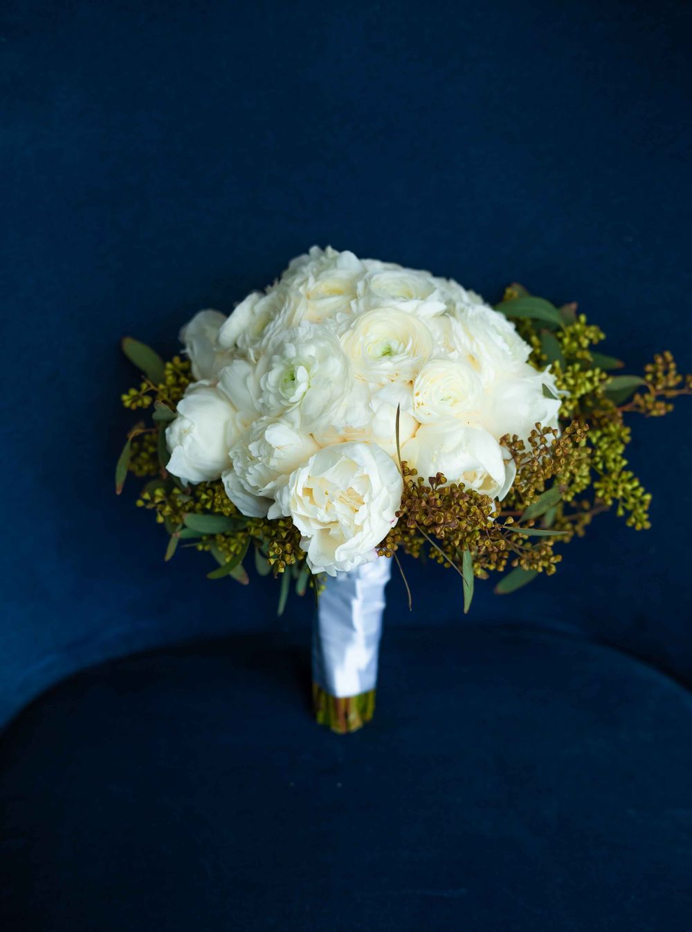 Elegant white rose bridal bouquet wrapped in satin ribbon against dark blue background.