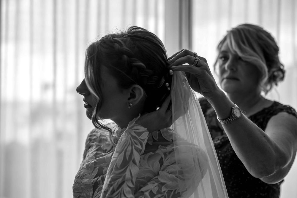A bride gets help adjusting her veil during wedding preparations in a black and white candid moment.