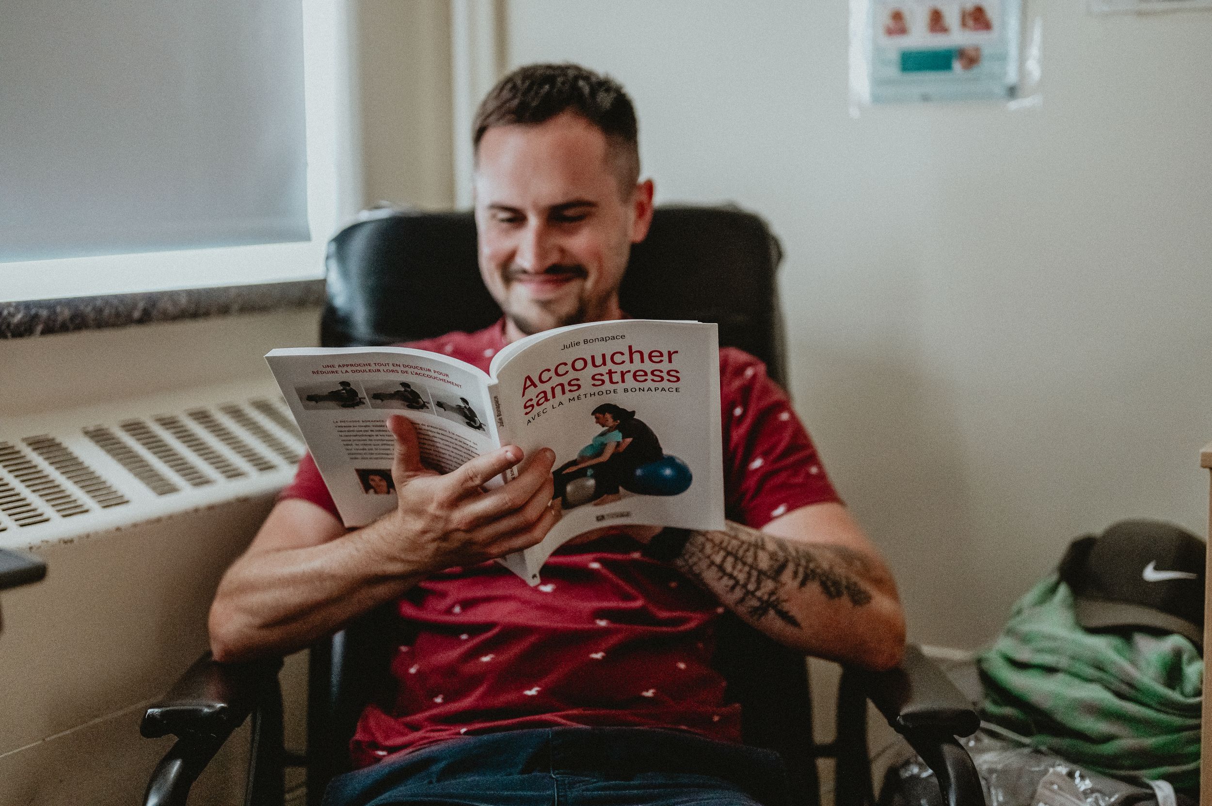 Person in red patterned t-shirt reading a book while relaxing in a comfortable indoor setting.