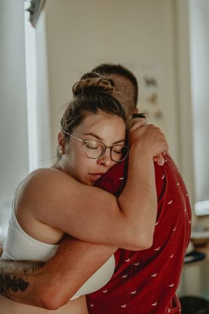 Intimate moment showing a gentle embrace between two people in a bright interior space.